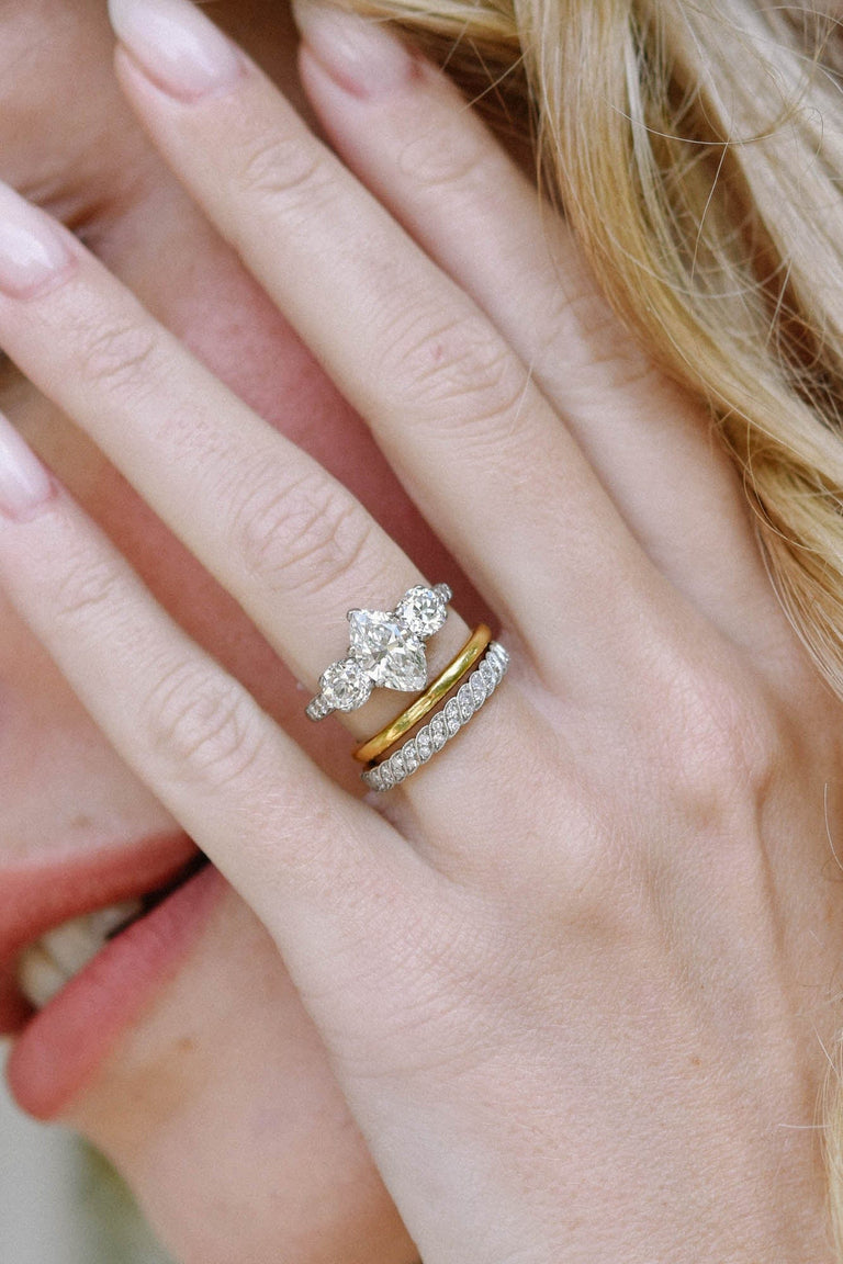 antique three stone diamond engagement ring paired with a gold band and eternity band on a women's hand held by her face