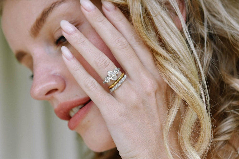 antique three stone diamond engagement ring paired with a gold band and eternity band on a women's hand held by her face