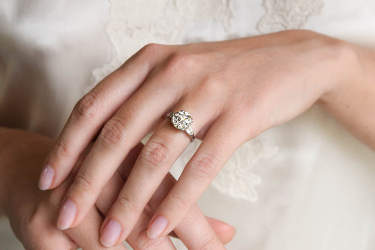 Close-up of a hand wearing a 3 carat antique diamond ring on a soft, blurred background