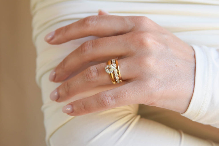 Hand wearing a custom gold engagement ring with a diamond on a beige background