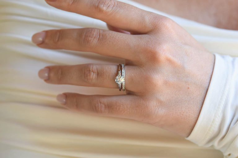 Hand wearing a platinum vintage inspired wedding band and engagement ring on a light background