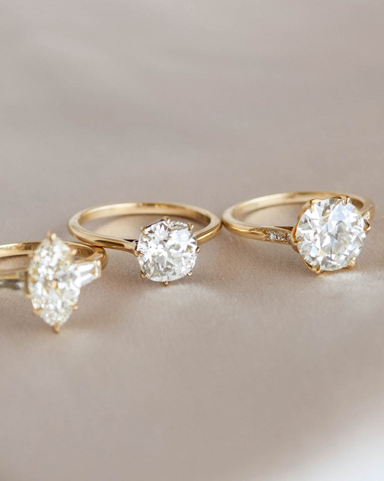 Three gold engagement rings with diamond stones on a light background